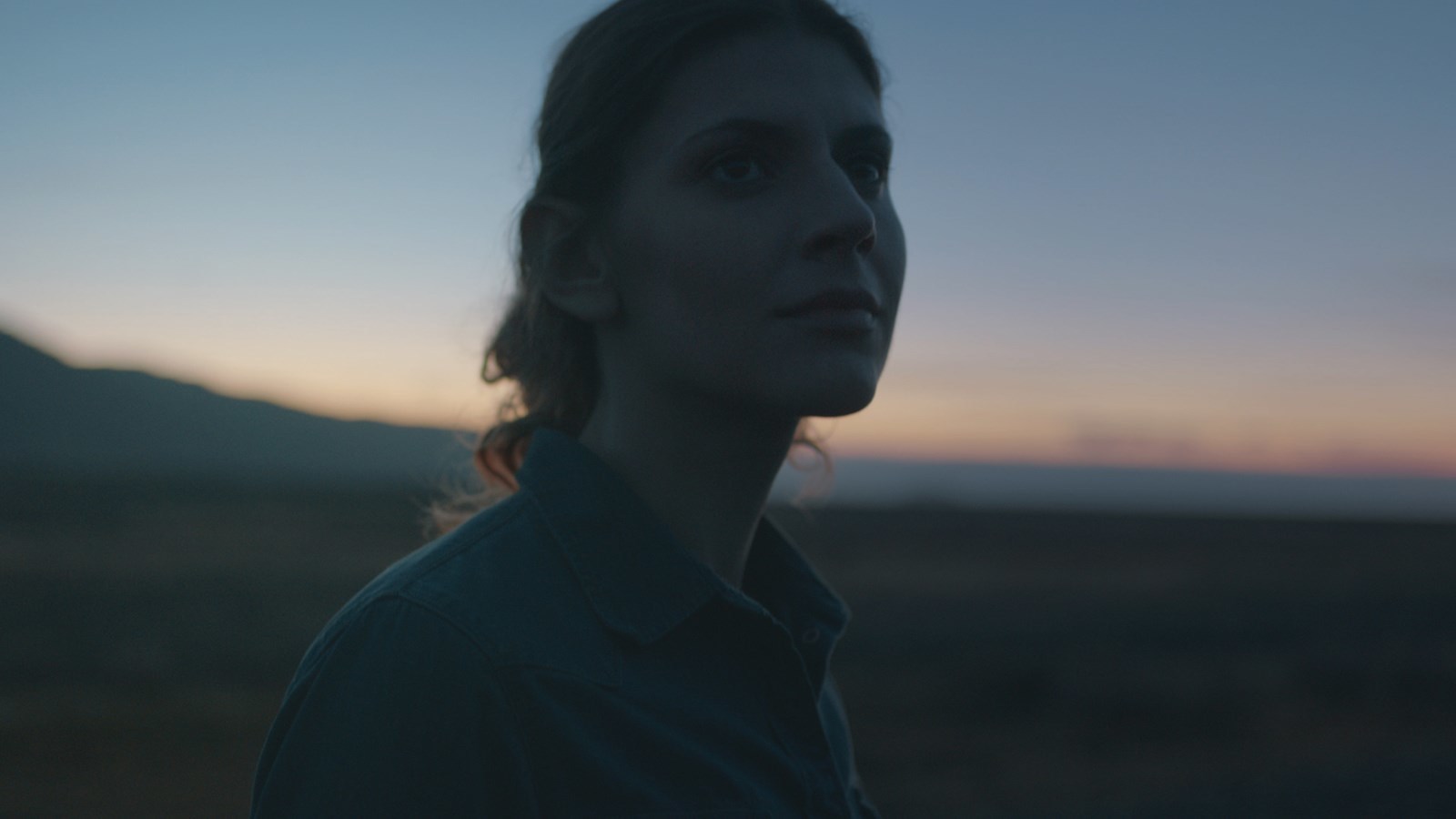 a woman standing in a field at sunset