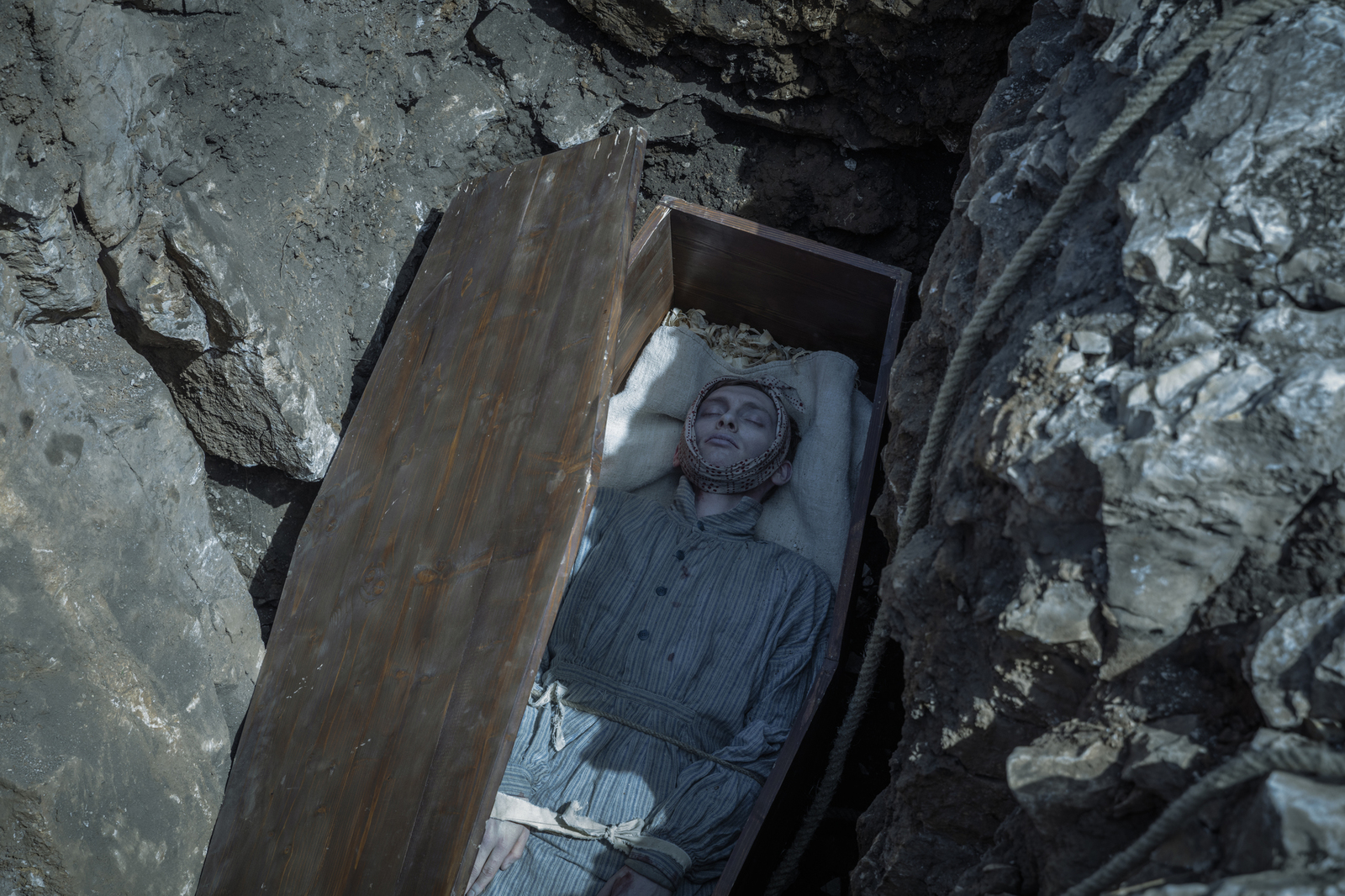 a man laying in a wooden box in a rocky area