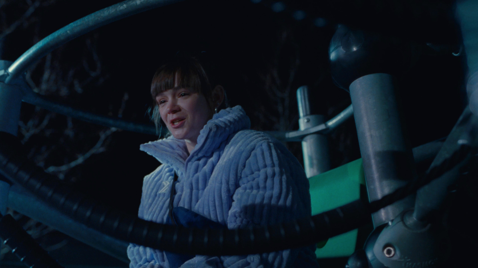 a woman in a blue jacket standing next to a metal pipe