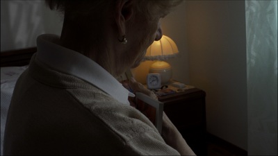 an older woman is reading a book in the dark