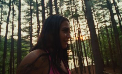 a woman standing in front of a forest at sunset