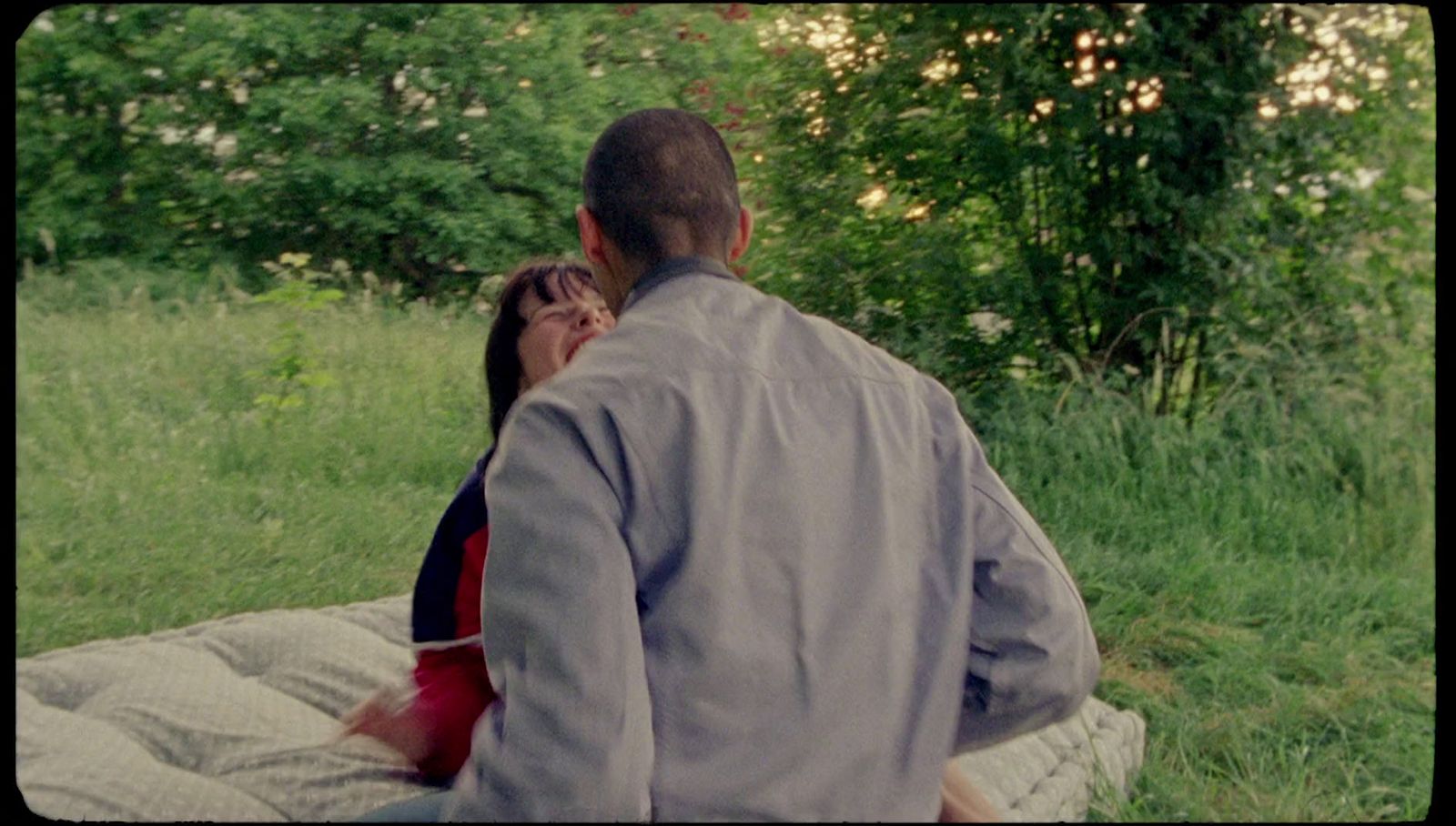 a man and woman sitting on a blanket in the grass