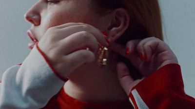 a woman wearing a red and white sweater putting on a pair of gold earrings