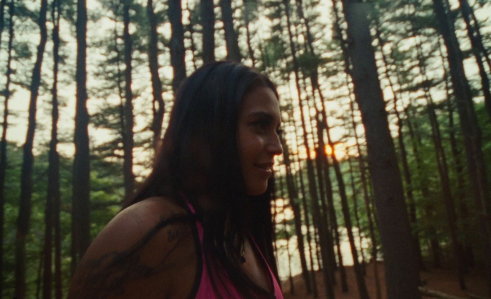 a woman standing in front of a forest at sunset