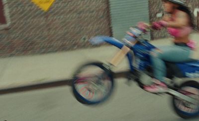 a woman riding a small blue motorcycle down a street