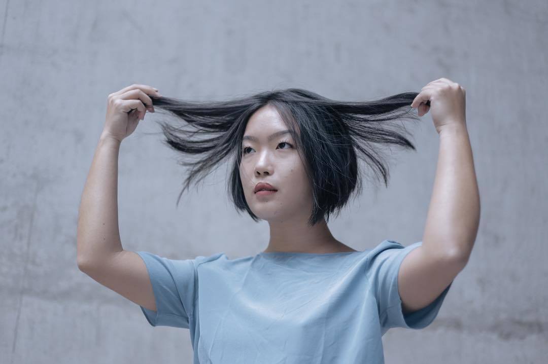 a woman with black hair holding her hair in the air