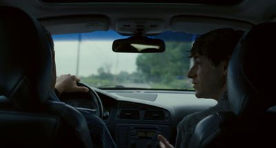 a man driving a car with another man talking on the phone