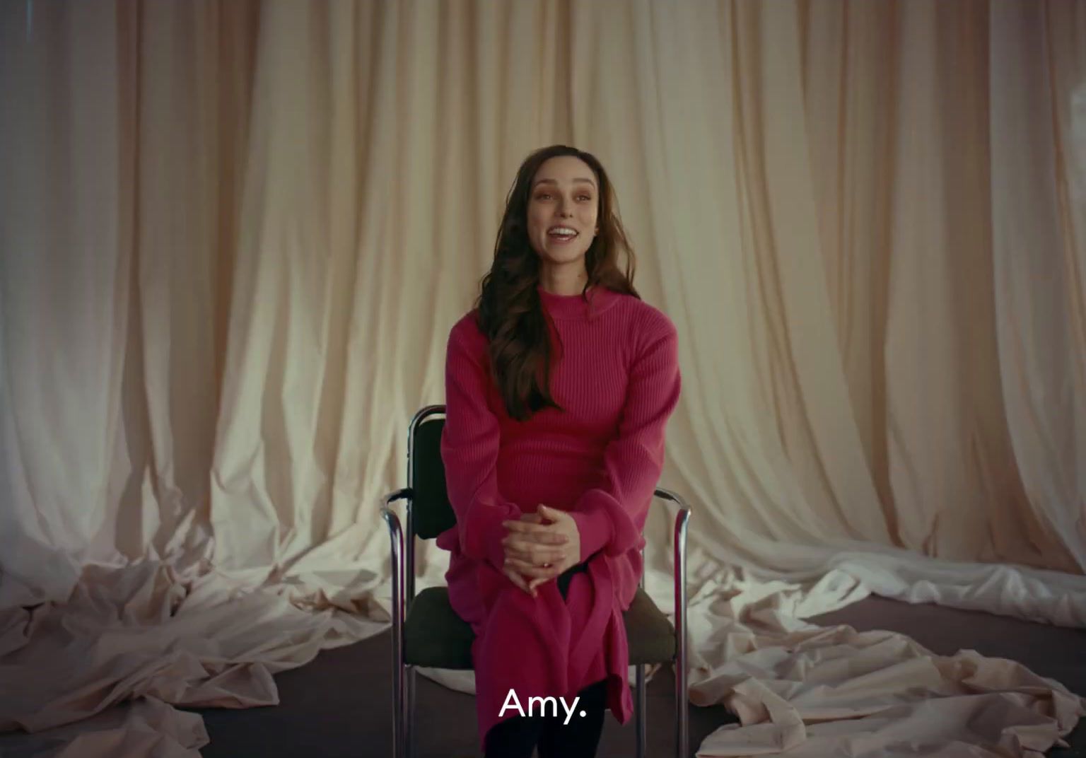 a woman sitting in a chair in front of a curtain