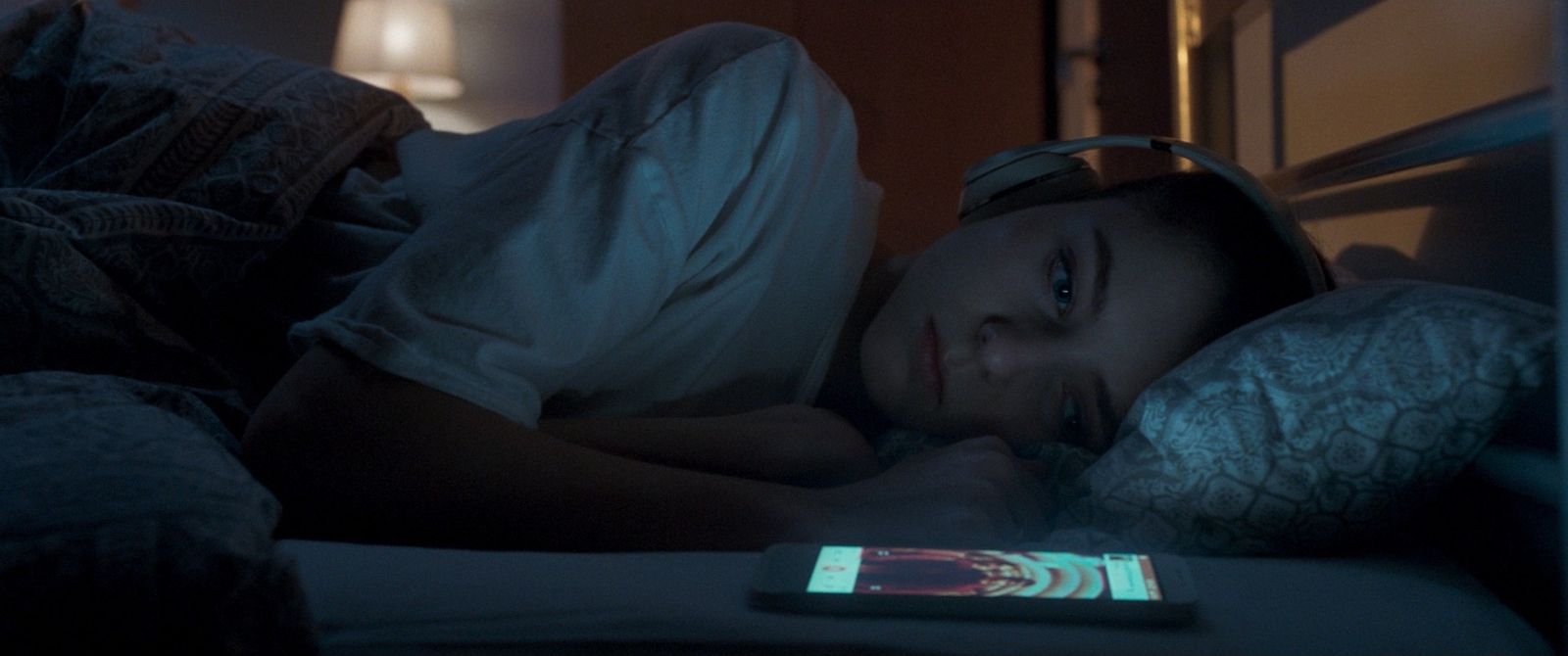 a young girl laying in bed with a cell phone