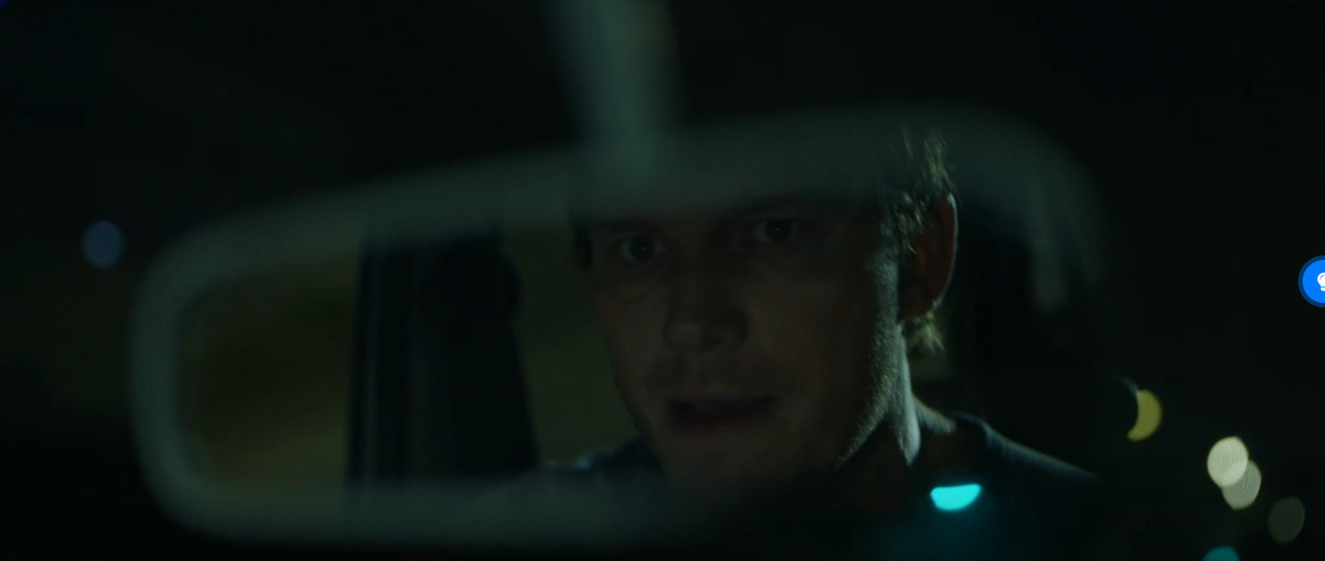 a man driving a car at night in the rear view mirror