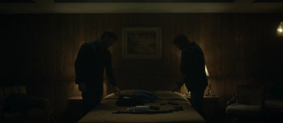 two men standing over a bed in a dark room