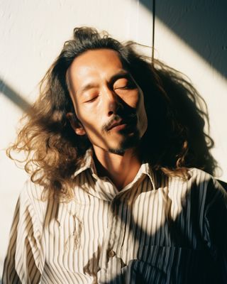 a man with long hair standing in front of a wall