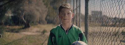 a young boy holding a soccer ball in front of a fence