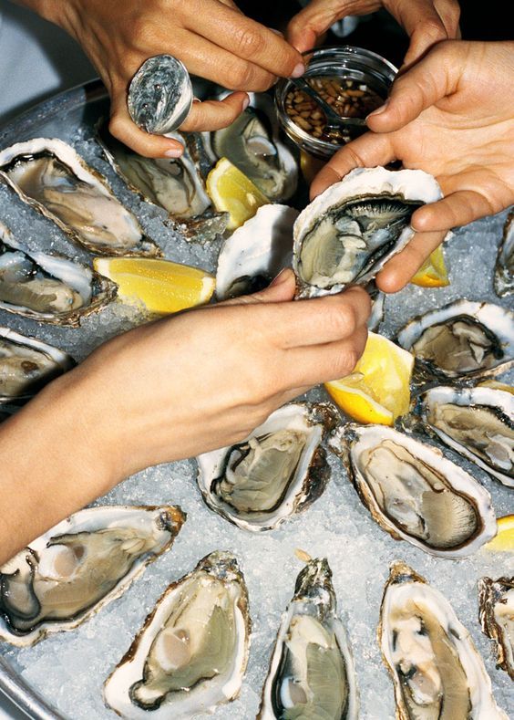 a group of people putting lemon wedges on a platter of oysters