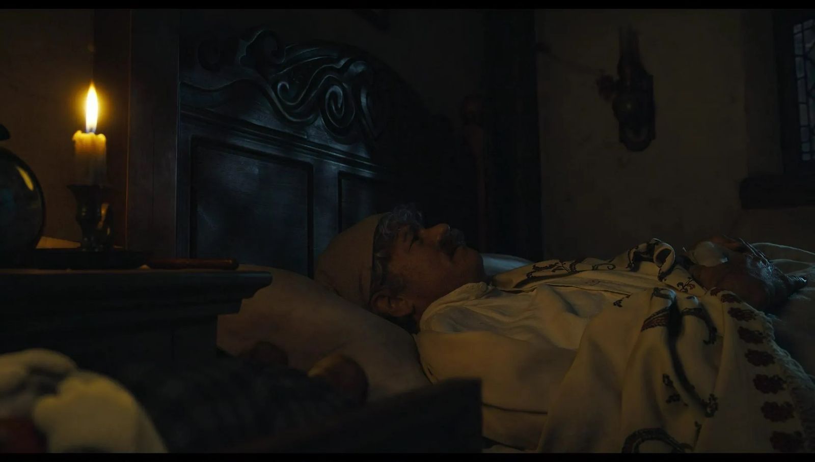 a man laying in bed next to a lit candle