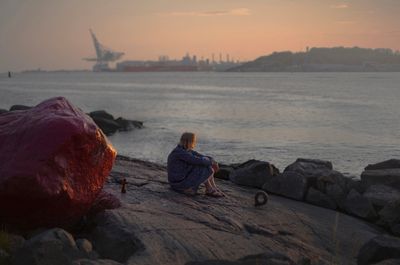 a woman sitting on a rock next to a body of water