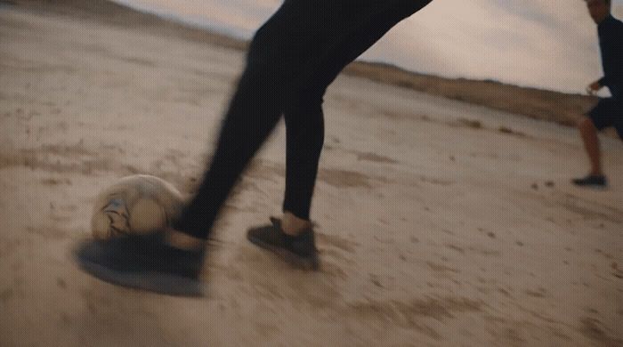 a man kicking a soccer ball on a sandy beach