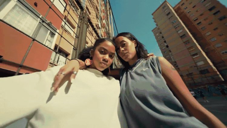 two women standing next to each other in front of tall buildings