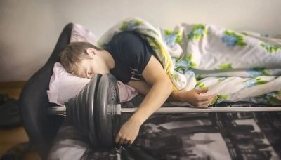 a young boy sleeping on a bed with a dumbbell