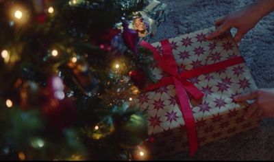 a person opening a christmas present under a christmas tree