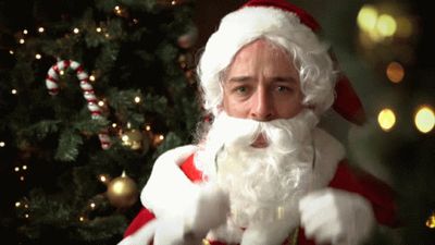 a man dressed as santa claus standing in front of a christmas tree