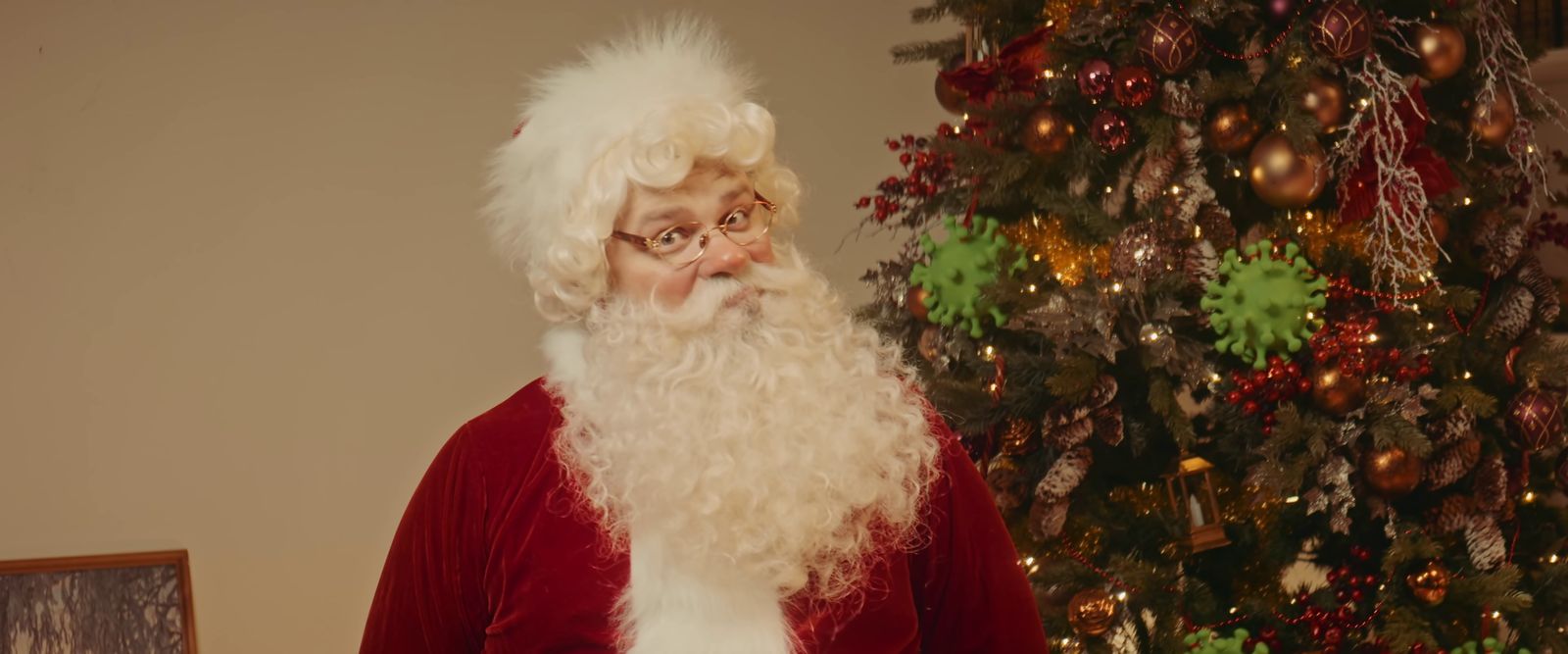 a man dressed as santa claus standing in front of a christmas tree