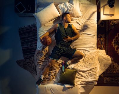 a man laying in bed with a basketball