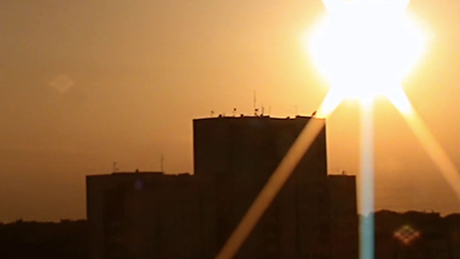 the sun is setting behind a tall building