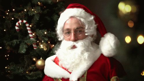 a man dressed as santa claus standing in front of a christmas tree