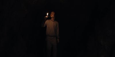 a man standing in the dark holding a lit candle