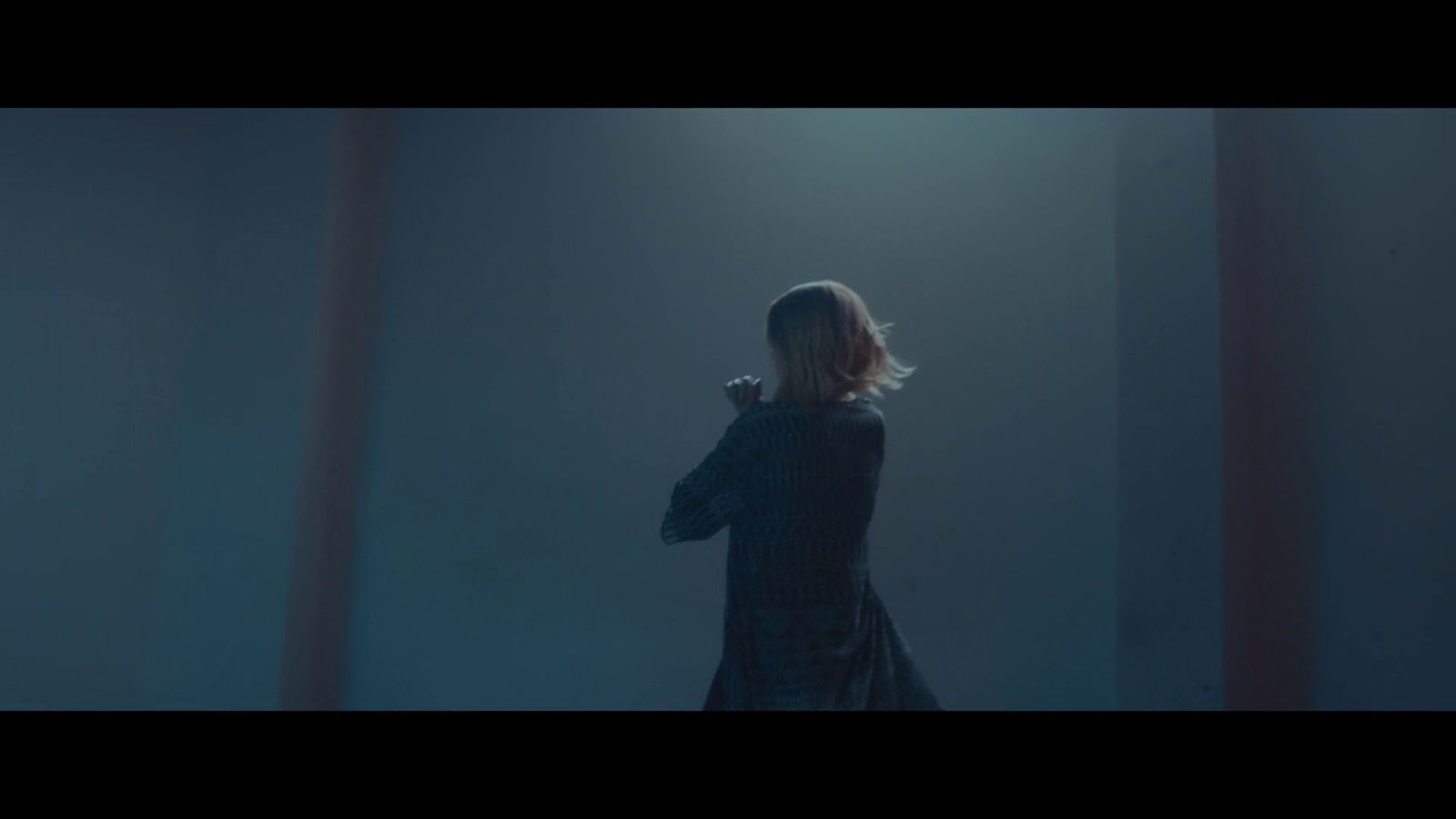 a woman standing in a dark room with her arms crossed