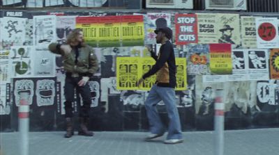 a man and a woman walking past a wall covered in posters