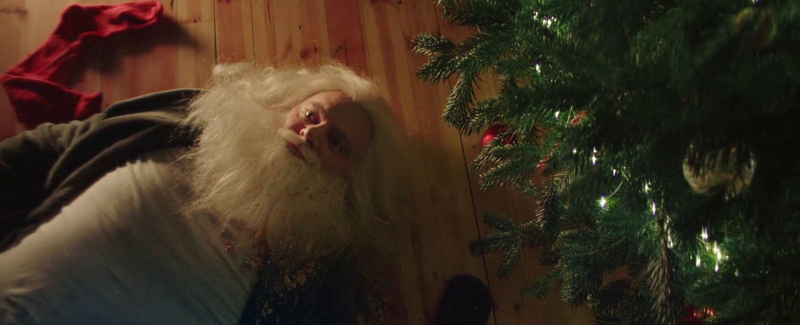 a man with long white hair and a beard laying next to a christmas tree