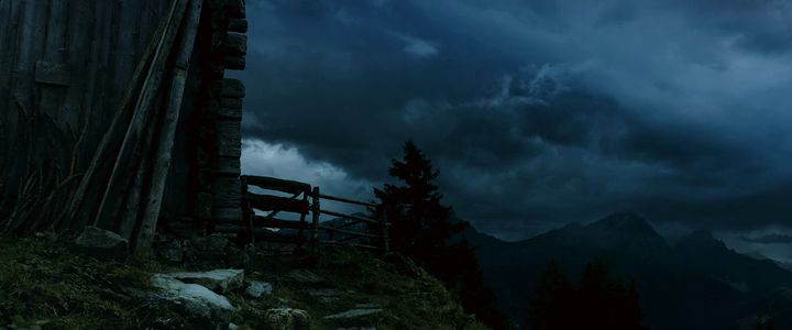 a wooden building sitting on top of a hill under a cloudy sky