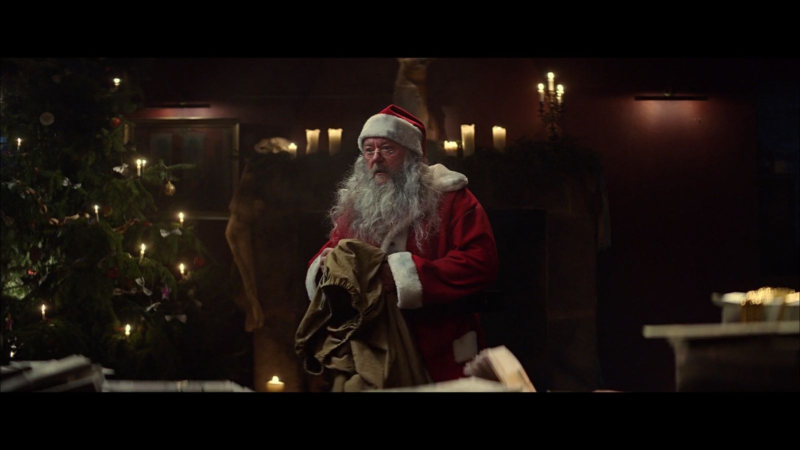 a man dressed as santa claus standing in front of a christmas tree