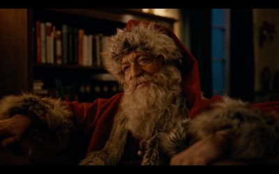 a man dressed as santa claus sitting in front of a book shelf