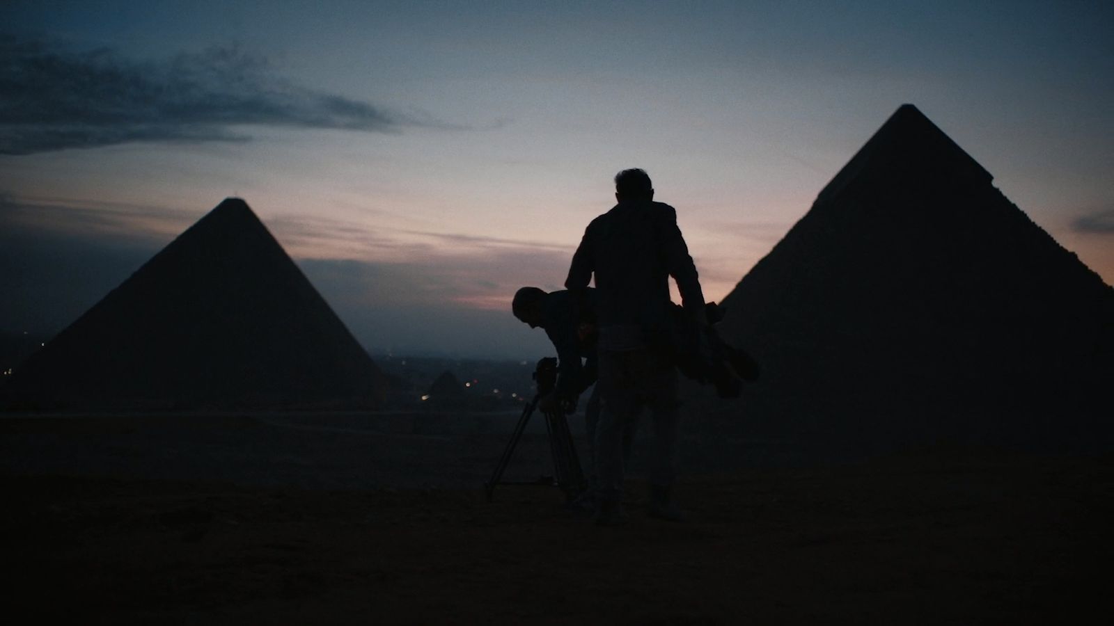 a man standing in front of two pyramids at night