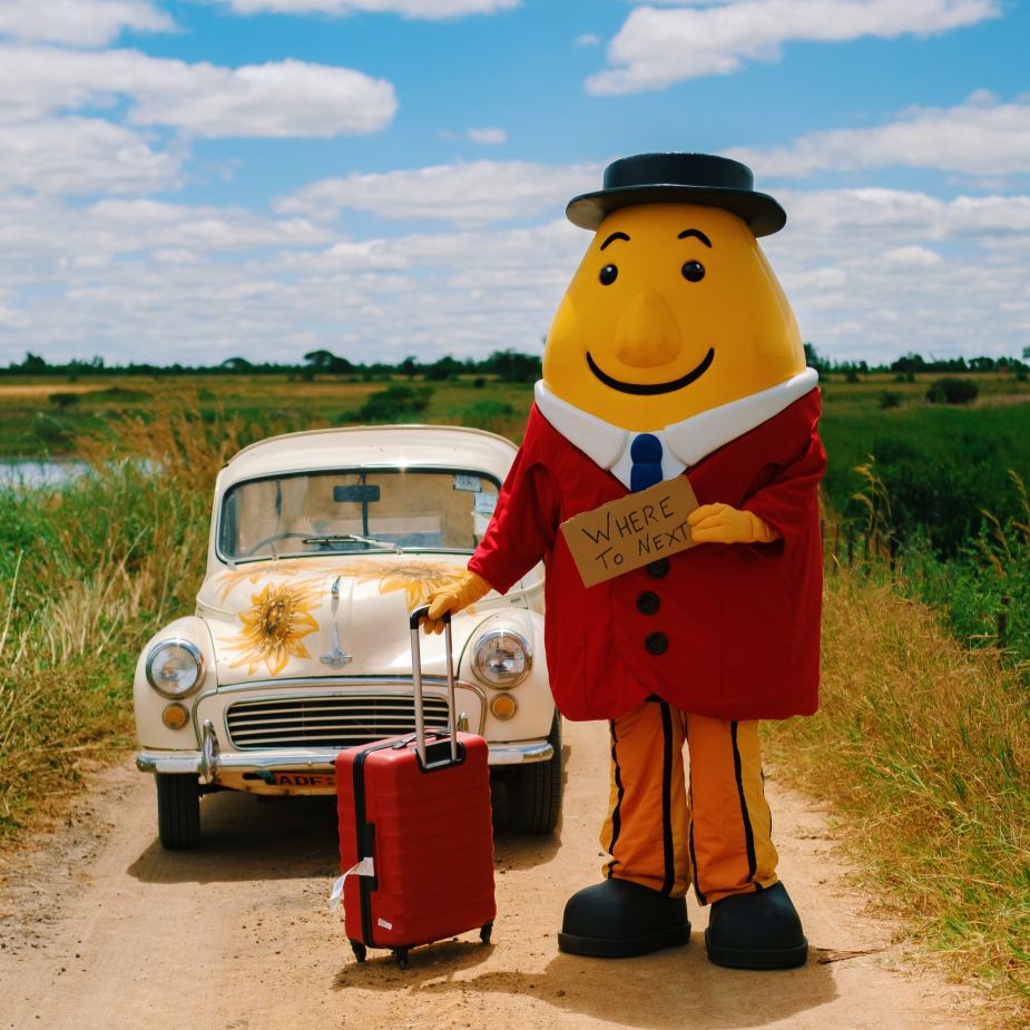 a large inflatable character with a suitcase and a car on a dirt road