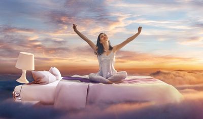 a woman sitting on top of a bed with her arms in the air