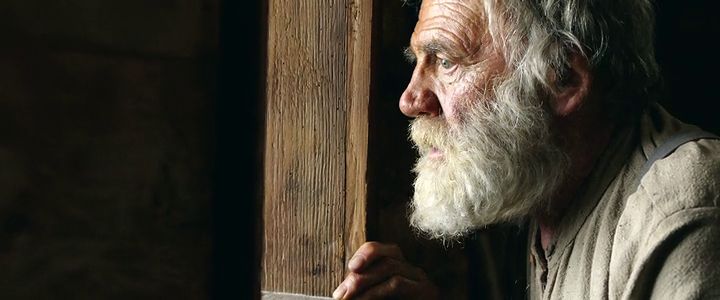 a man with a long white beard looking out a window