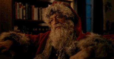 a man dressed as santa claus sitting in front of a book shelf