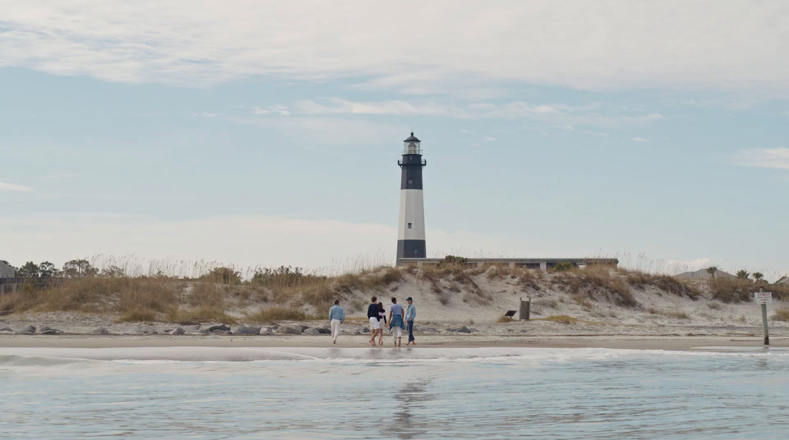 a group of people walking on a beach next to a light house