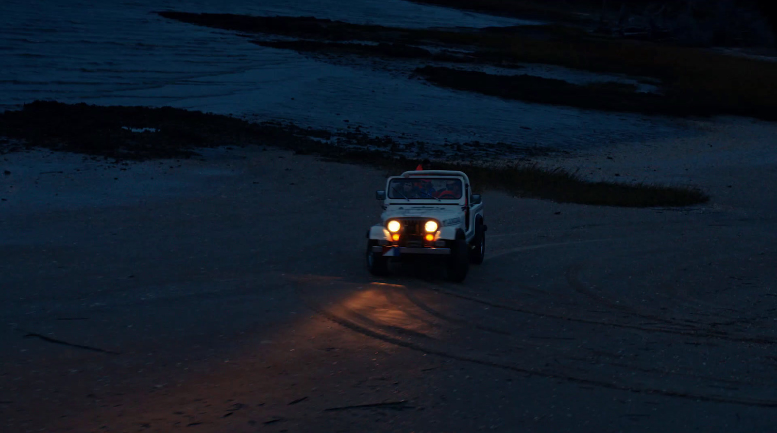 a jeep driving down a beach at night