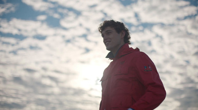 a man in a red jacket standing in front of a cloudy sky