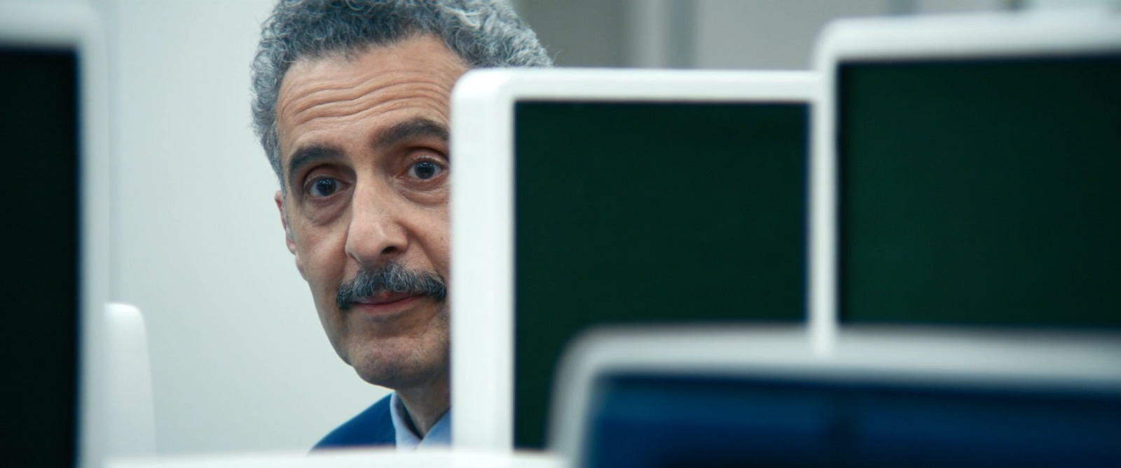 a man with a mustache looking at a computer monitor