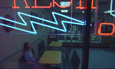 a woman sitting at a table in front of a neon sign