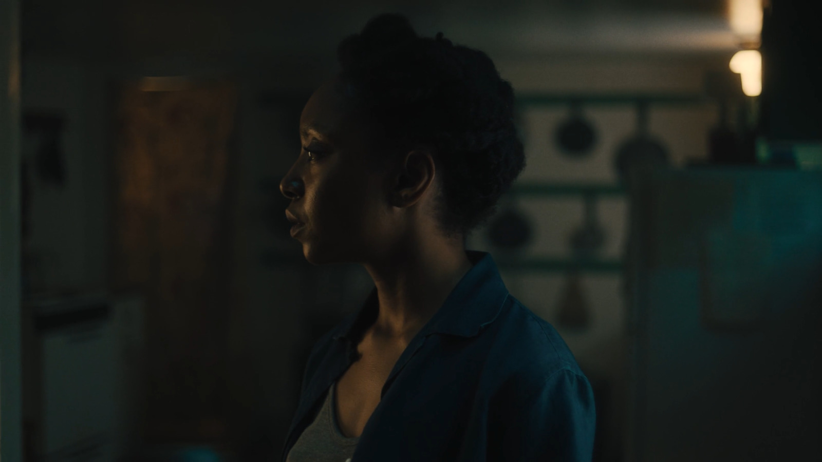 a woman standing in a dark kitchen looking off into the distance