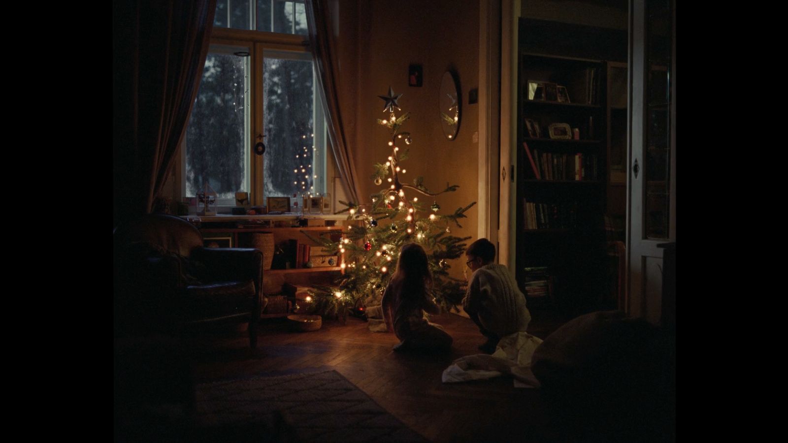 two people sitting on the floor in front of a christmas tree