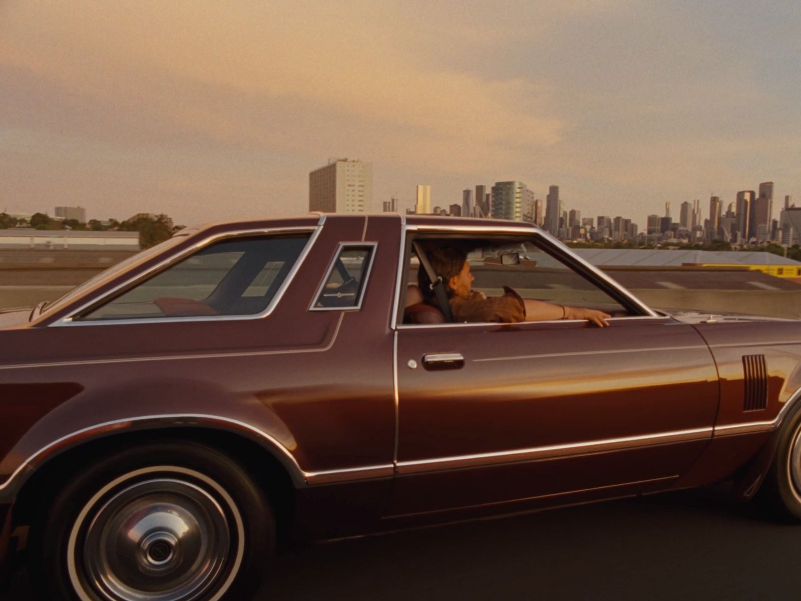 a brown car driving down a street next to tall buildings