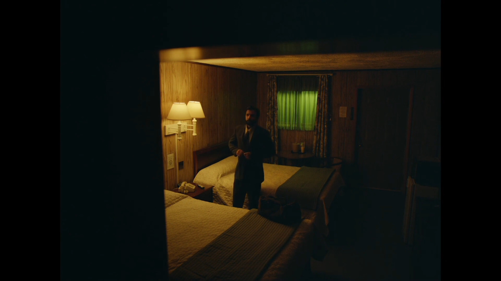 a man standing in a dark room next to two beds